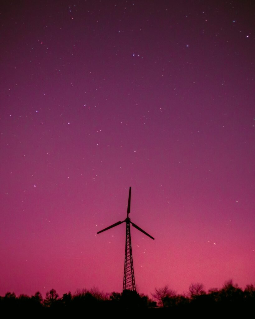 Wind turbine silhouette with a vibrant purple sky and stars, symbolizing renewable energy.