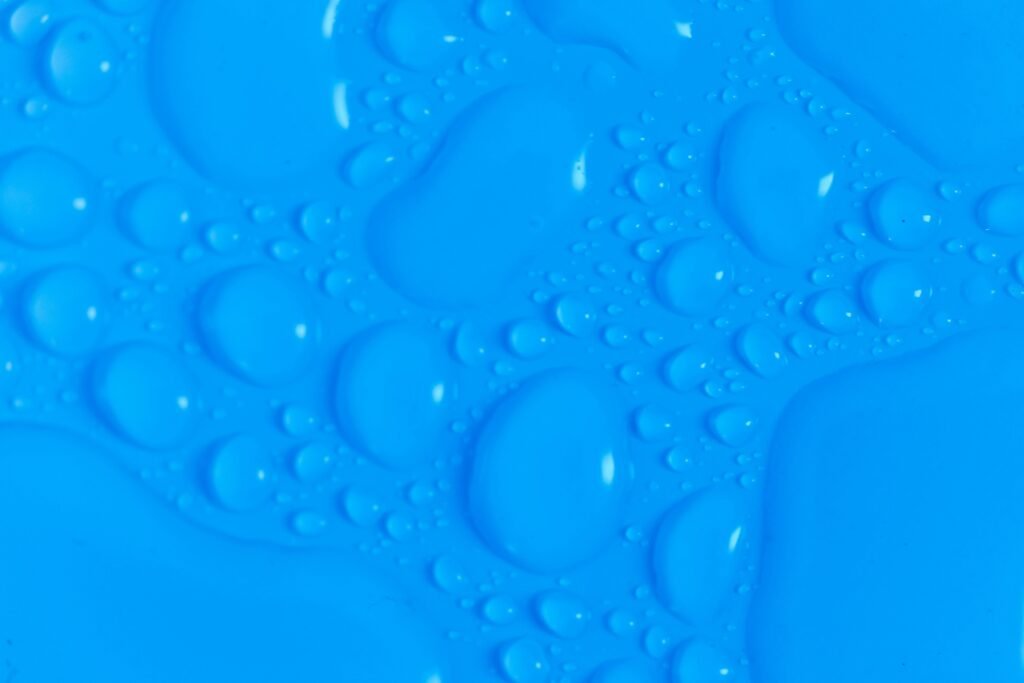 Closeup top view of dark blue wet blurred background with still shiny abstract transparent fluid drops of different sizes and shapes