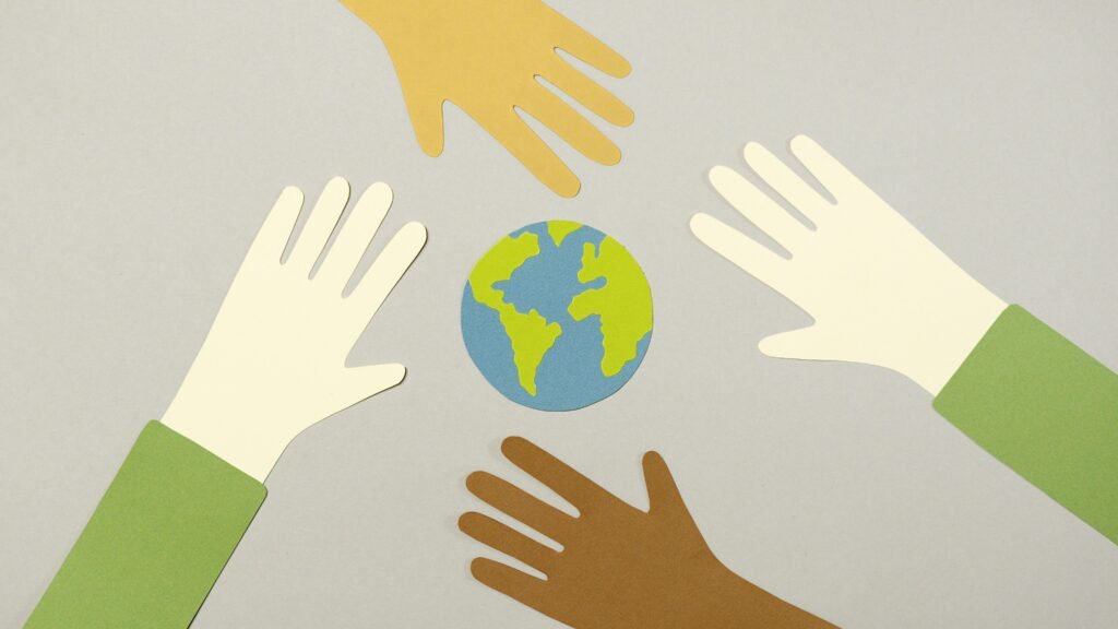 Colorful paper cutouts of diverse hands surrounding a small paper Earth, symbolizing unity.